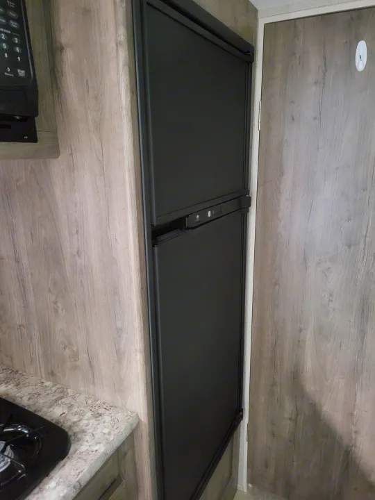 RV rental interior with wood-look surfaces, built-in microwave, stovetop, and black folding blackout panels.. Aspen Trail LE 2020