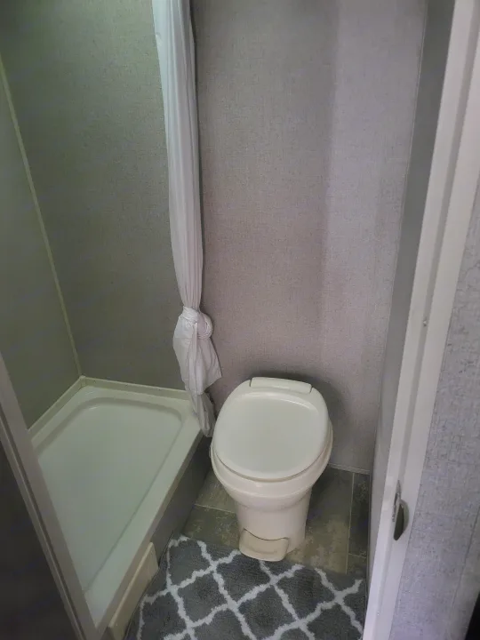 Compact RV rental bathroom with a white toilet, shower stall, and tied-back shower curtain. Practical space for your travels.. Aspen Trail LE 2020