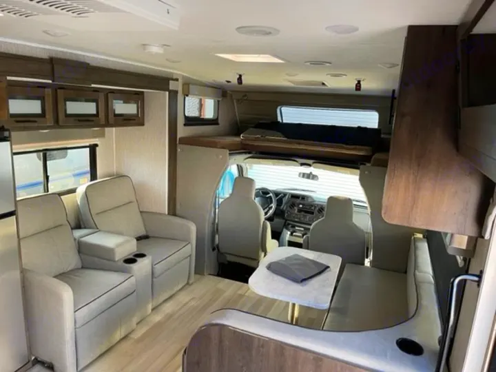 Spacious rv rental interior showing living area with recliners, dining table, front cab, and overhead bunk.. COACHMEN LEPRECHAUN 2021
