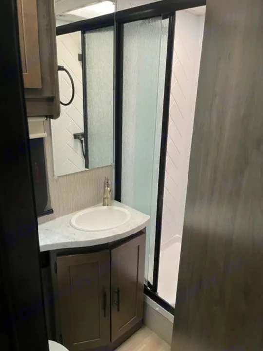 RV rental interior: Compact bathroom/kitchenette with a modern sink, dark cabinet, and pull-down window shade over a white tiled wall.. COACHMEN LEPRECHAUN 2021