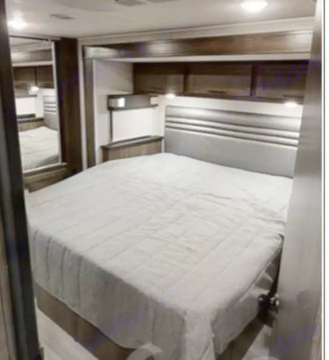 RV rental bedroom: a comfortable bed with gray comforter, overhead storage, and mirrored wardrobe on the left.. COACHMEN LEPRECHAUN 2021