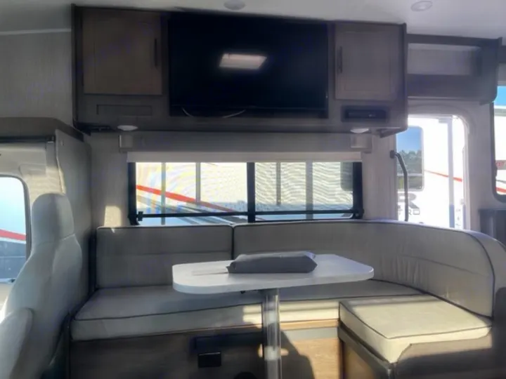 Cozy RV rental interior with a U-shaped dinette, table, overhead cabinets, and TV, designed for comfortable travel.. COACHMEN LEPRECHAUN 2021