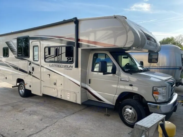 Spacious Class C Coachmen Leprechaun RV parked, ideal for rv rental adventures. A silver Airstream travel trailer is seen behind it.. COACHMEN LEPRECHAUN 2021
