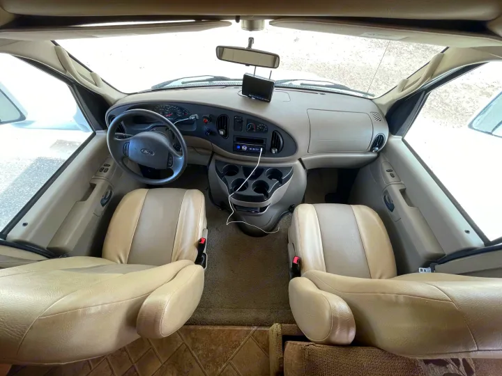 Spacious RV rental cockpit. Features beige driver/passenger seats, steering wheel, and dashboard, ready for journeys.. Forest River Sunseeker 2009