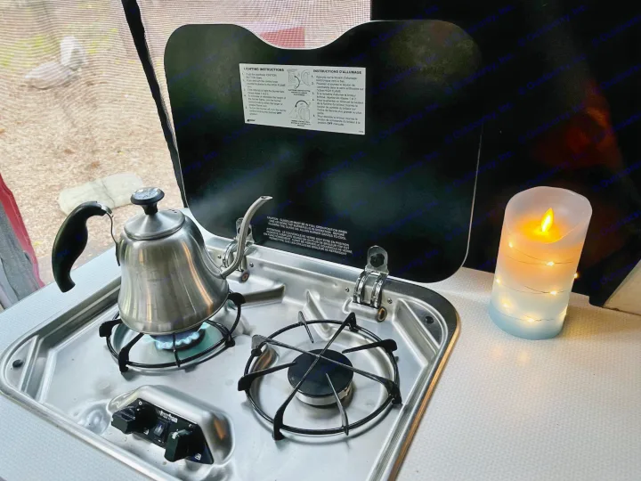 An RV rental kitchen: A kettle boils on a lit gas stove, with cooking instructions on the open cover and a cozy LED candle nearby.. Winnebago Solis 2021