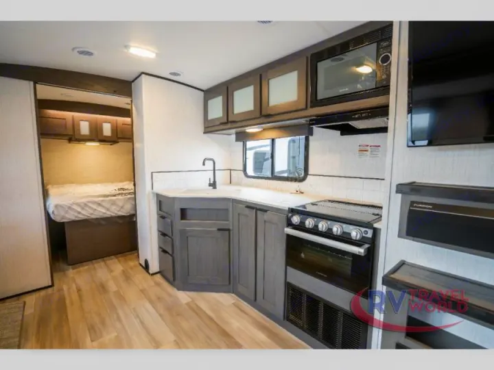 This modern RV rental features a compact, well-equipped kitchen with a stove, microwave, and sink, next to a cozy bedroom.. Cruiser RV MPG Ultra Lite 2022