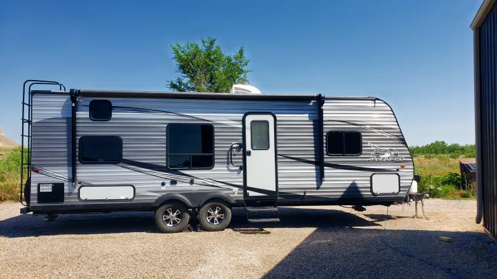 A sleek gray travel trailer, possibly an RV rental, is parked on a gravel lot under a clear blue sky, ideal for adventures.. Jayco Jay Flight SLX 2019