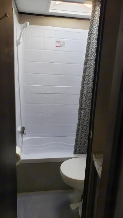 Inside an RV rental: a compact bathroom with a white shower/tub, toilet, and patterned shower curtain.. Jayco Jay Flight SLX 2019