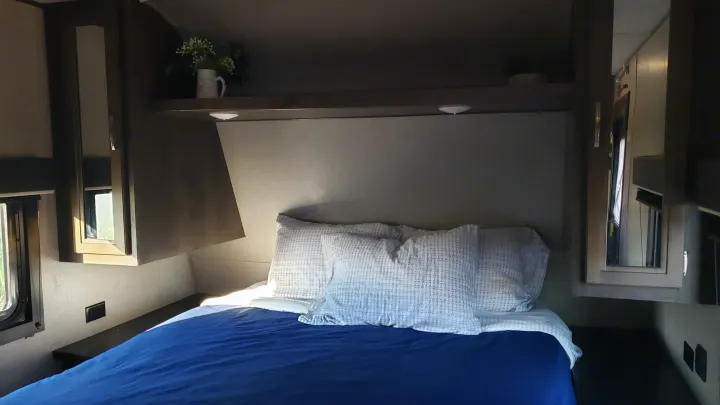 Interior view of an RV rental bedroom with a neatly made bed, overhead cabinets, and small windows for natural light.. Jayco Jay Flight SLX 2019