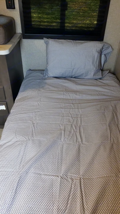 A neatly made bed with patterned sheets and pillow inside an RV rental, set against a window with blinds.. Jayco Jay Flight SLX 2019