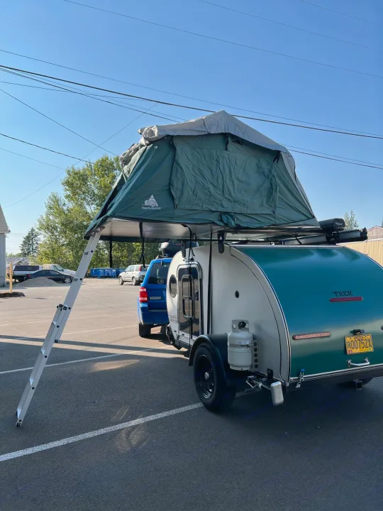 This RV rental setup features a teardrop camper with a large rooftop tent & ladder, ready for adventure camping.. Teardrops Northwest Trek 2022