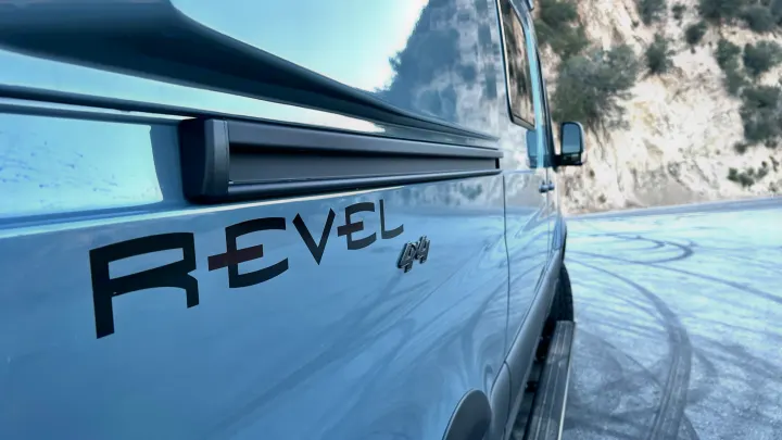 A light gray Winnebago Revel 4x4 camper van RV rental on a snowy road with mountains in the background.. Winnebago Revel 2022