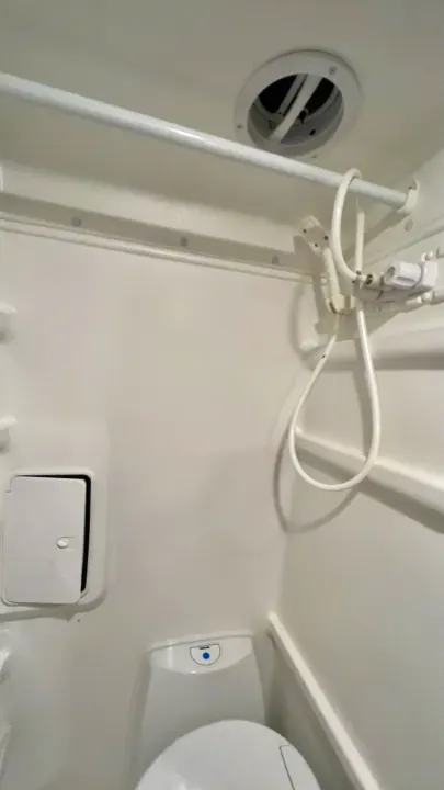 Inside this compact RV rental bathroom: an all-white design with a toilet, handheld shower, and ceiling vent.. Winnebago Revel 2022