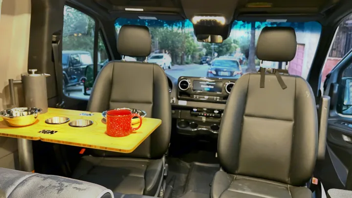 Cozy RV rental interior with swiveling front seats, a versatile table, and coffee setup. Perfect for camper van adventures.. Winnebago Revel 2022