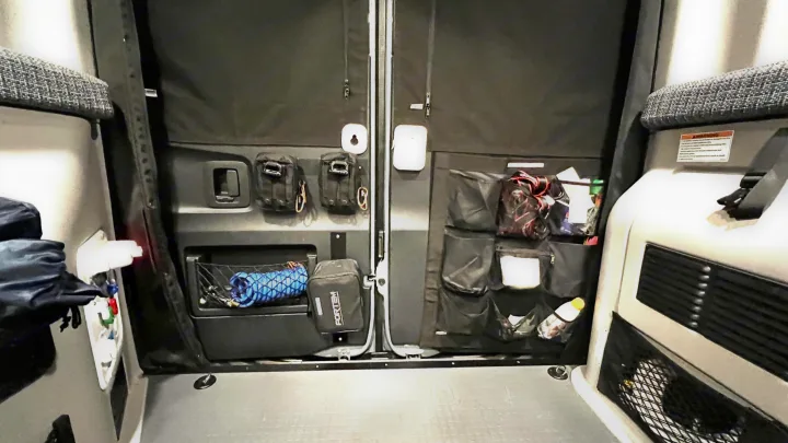 RV rental interior: organized rear doors with blackout shades. Various storage includes tactical pouches, nets, and multi-pocket organizers.. Winnebago Revel 2022