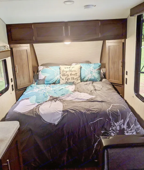 Cozy RV rental bedroom, featuring a comfy bed with floral bedding, overhead storage, and side windows.. Forest River Cherokee Wolf Pup 2019