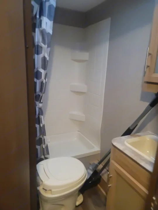 Compact rv rental bathroom featuring a shower with a patterned curtain, toilet, and sink vanity. Cleaning supplies are visible.. Coachmen Other 2021