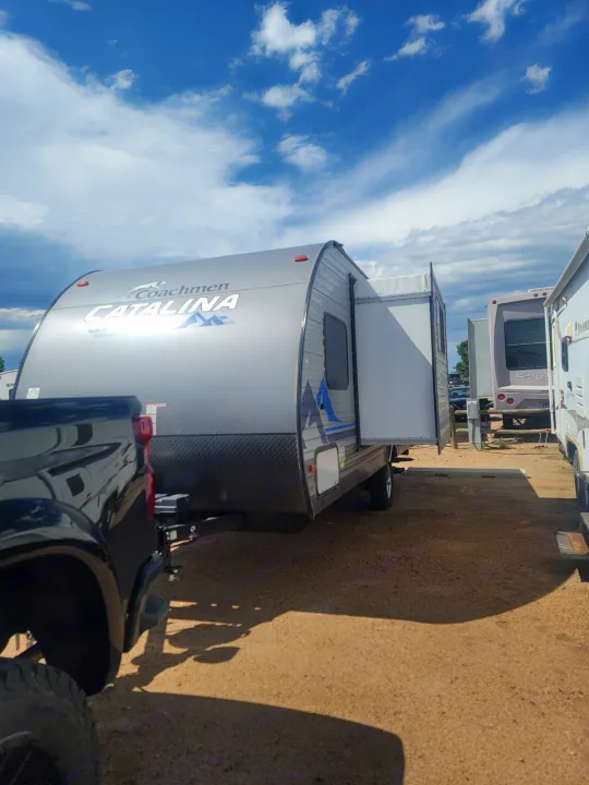 Coachmen Catalina travel trailer RV rental hitched to a black truck. Slide-out extended, parked on a dirt lot under a cloudy sky.. Coachmen Other 2021