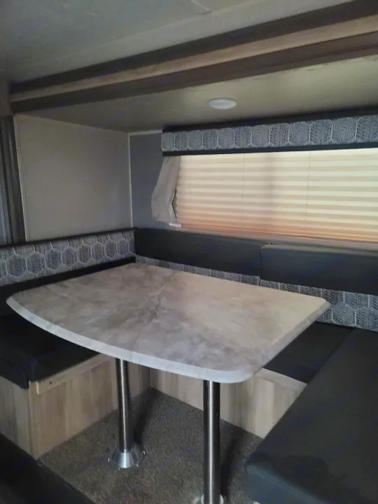 Spacious RV rental dinette with a light-colored table, geometric-patterned bench seating, and window blinds.. Coachmen Other 2021