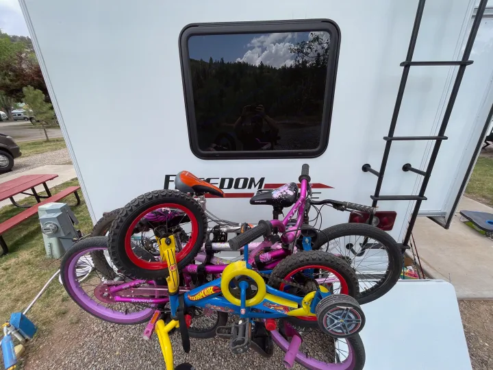 Colorful bikes mounted on an RV rental for a family camping adventure. Window reflects scenic outdoors and photographer.. Thor Freedom Elite 2020