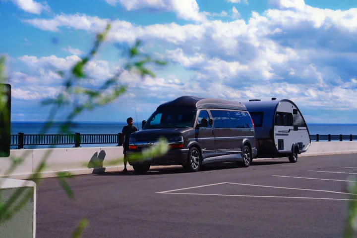 Scenic view with a man standing by his RV rental van and teardrop trailer by the ocean.. Nucamp Tab 400 2022