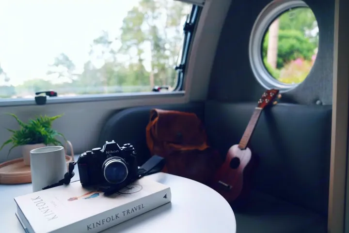 Cozy RV rental interior with a travel camera, Kinfolk book, ukulele, and plant. Nature views from the windows.. Nucamp Tab 400 2022