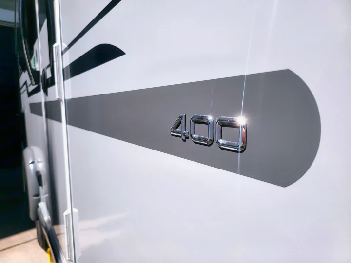 Detailed view of an RV side with shiny chrome '400' numbers on a grey graphic stripe, ideal for your RV rental adventure.. Nucamp Tab 400 2022