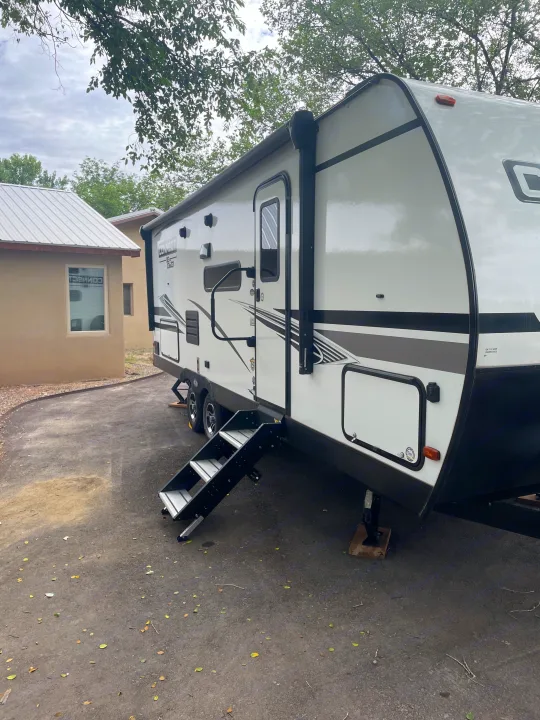 White and black rv rental travel trailer parked with steps extended, next to a building under a cloudy sky.. Connect SE 2021