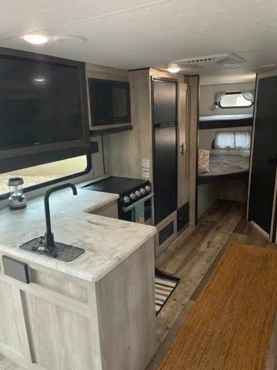 Explore this cozy RV rental interior featuring a well-equipped kitchen, TV, and comfortable bunk beds for travel.. Connect SE 2021