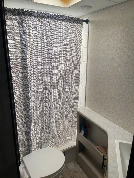 Clean RV rental bathroom with a patterned shower curtain, toilet, and vanity storage for comfortable travel.. Connect SE 2021