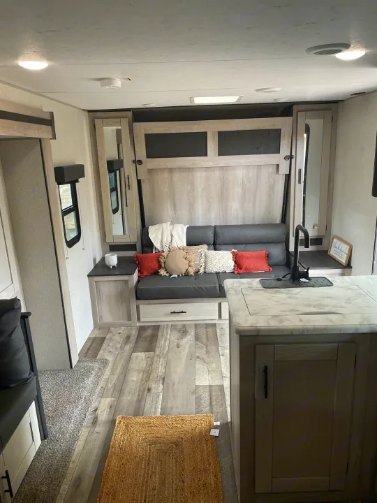 Modern rv rental interior with light wood and grey tones, featuring a compact kitchen island, convertible sofa, and homey accents.. Connect SE 2021