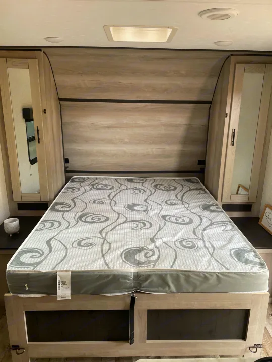 An RV rental bedroom with a grey and white patterned mattress, flanked by light wood cabinets with mirrors, and overhead lighting.. Connect SE 2021