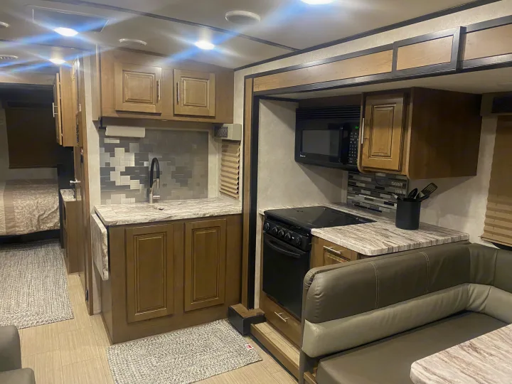 Well-equipped RV rental interior showcasing a modern kitchen with a sink, stove, microwave, and adjacent dining area with booth seating.. FR3 FR3 Motorhome 2020