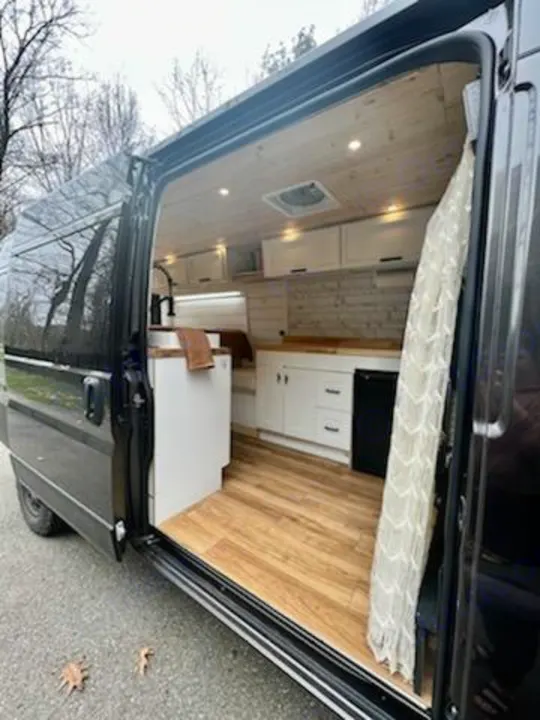 This RV rental camper van interior features a well-equipped kitchen, wood floor, and bright lighting for your travels.. Dodge Ram 3500 Pro master 2022