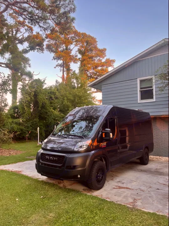 Adventure awaits! Dark gray RAM ProMaster camper van, ideal for rv rental, parked in a driveway. House & trees behind.. Dodge Ram 3500 Pro master 2022