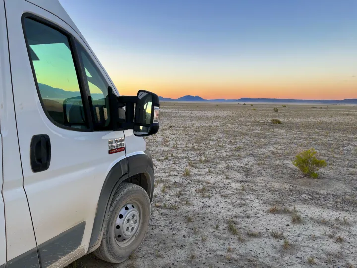 White Ram ProMaster RV rental parked in a vast, dry desert landscape at sunset, showcasing remote van life.. RAM ProMaster 2022