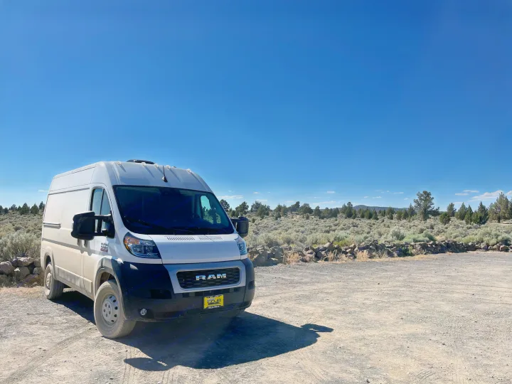 White Ram ProMaster camper van, ideal for an RV rental, on a sunny dirt parking area in an open desert landscape.. RAM ProMaster 2022