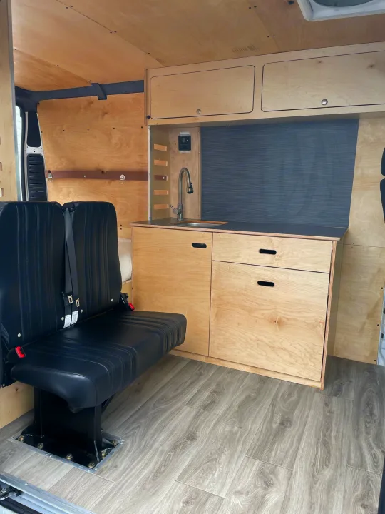 Inside an **rv rental**: clean **van conversion** with comfy seating, full **kitchenette**, wood cabinets, & durable flooring.. RAM ProMaster 2022