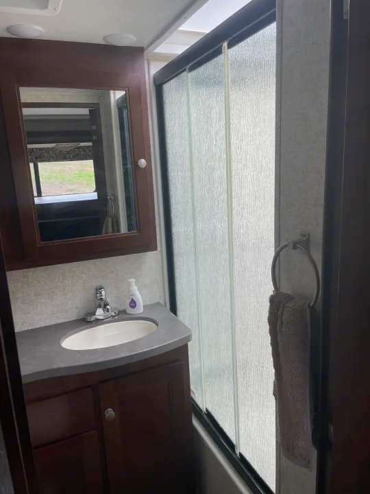 Inside this rv rental, find a clean, compact bathroom with a vanity, sink, mirror, and frosted glass shower for your travels.. Forest River Sunseeker 2017
