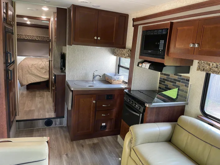 RV rental interior: Full view of a modern kitchen with stove, microwave, sink, and adjacent sofa, leading to a bedroom.. Forest River Sunseeker 2017
