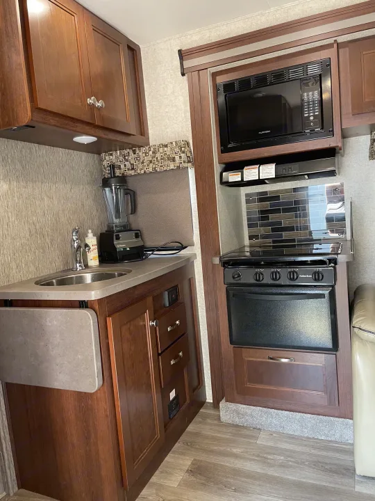 Compact RV rental kitchen with dark wood cabinets, sink, microwave, and stove for convenient meal prep on the road.. Forest River Sunseeker 2017