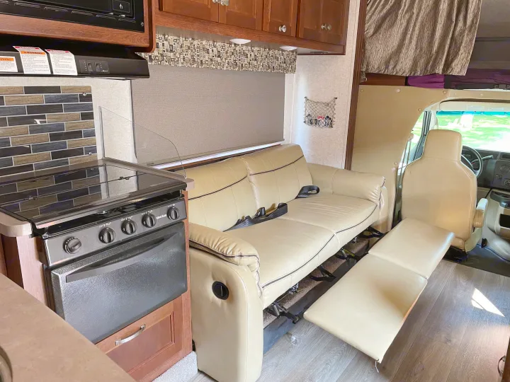 Modern RV rental interior: kitchen with stove, and a light-colored sofa extended for comfort or sleeping.. Forest River Sunseeker 2017