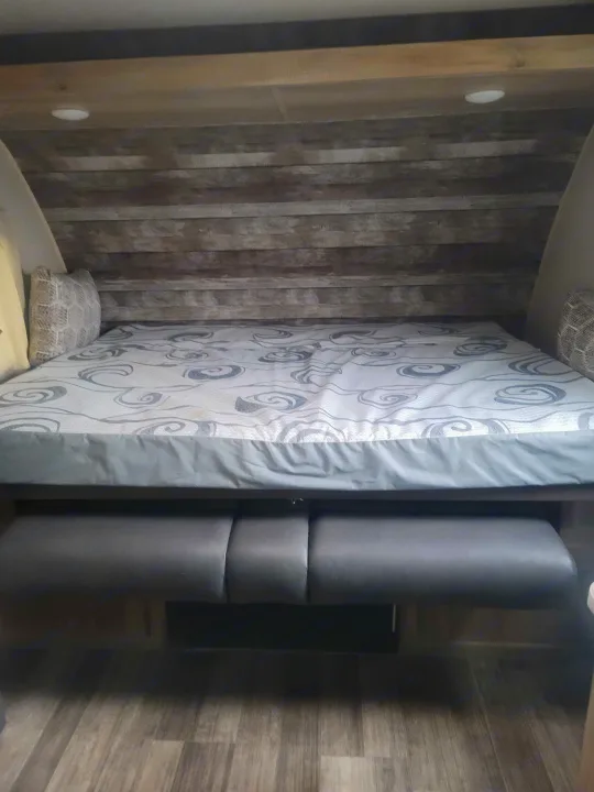 RV rental interior: a bed with patterned mattress, wood panel wall, overhead lights, and dark bench seating.. Coachmen Other 2021