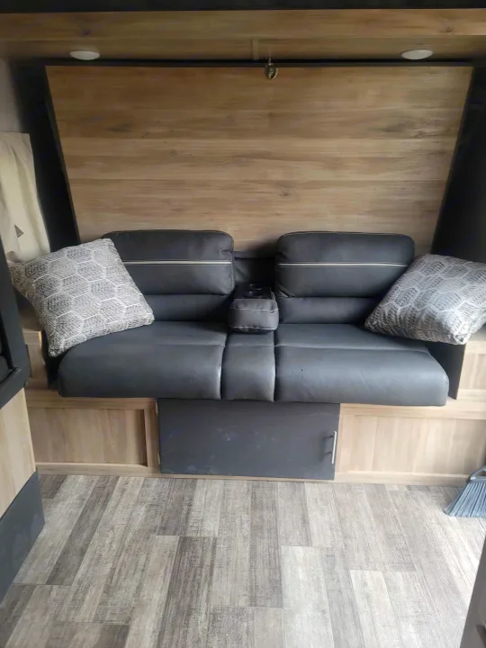 Cozy dark gray sofa with cupholders and pillows in an rv rental, featuring wood-look paneling and light flooring.. Coachmen Other 2021