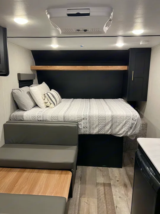 Modern RV rental interior: cozy bed with patterned bedding, dinette, and compact living space for travel.. Keystone Springdale 2022