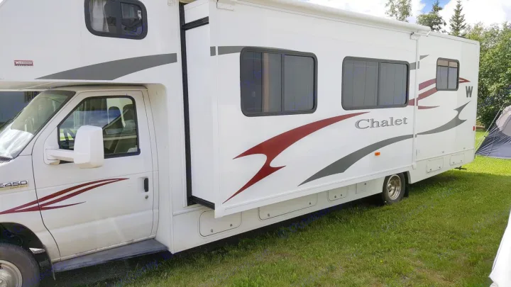 White Winnebago Chalet Class C RV rental with its slide-out extended, parked on a grassy site.. Winnebago Chalet 2013