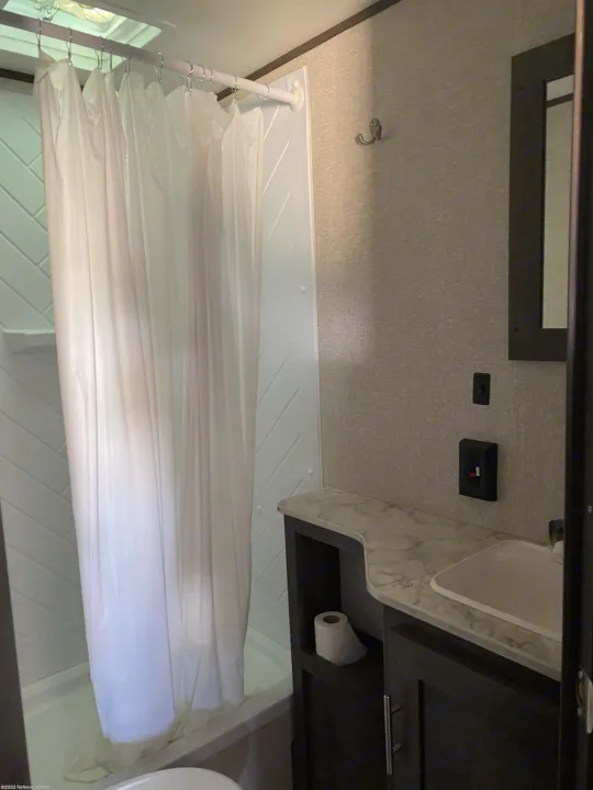 Inside an RV rental bathroom, featuring a shower with a white curtain, a vanity with a sink, and integrated storage.. Dutchmen Coleman Lantern LT 2022