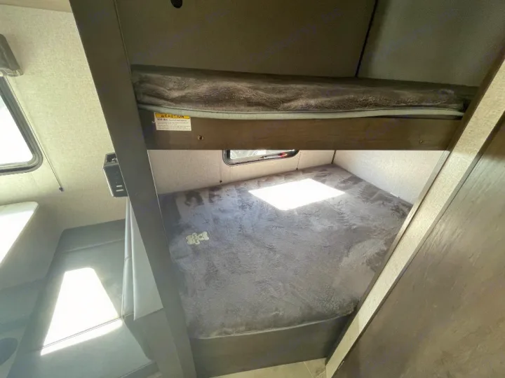 RV rental interior: two comfortable bunk beds provide a cozy sleeping area. Sunlight streams through windows, illuminating the space.. Dutchmen Coleman Lantern LT 2022