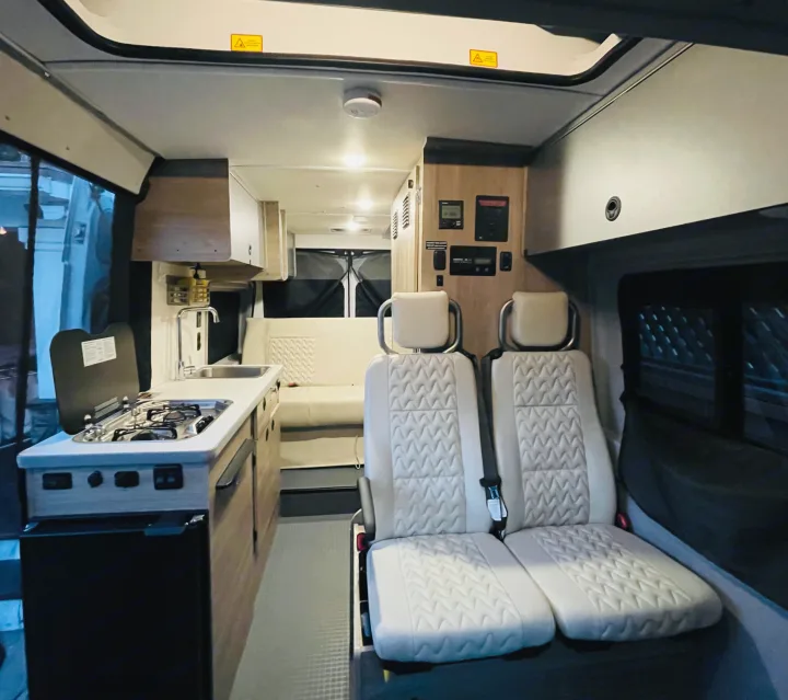 Modern RV rental interior: kitchenette with stove & sink, twin quilted seats, rear lounge area, and control panel.. Winnebago Winnebago 2023