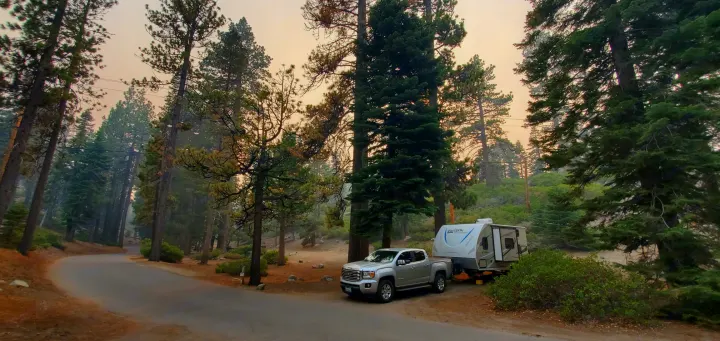 A silver truck with an RV rental is parked under a hazy, orange sky among tall forest trees. A serene camping scene.. Coachmen Other 2019